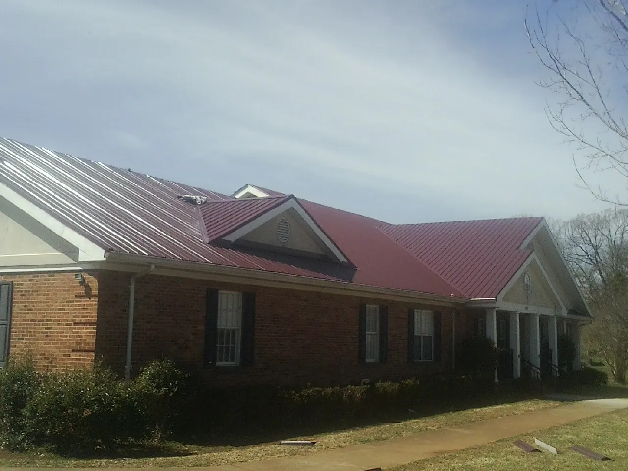Red metal roof with gabled entries on a long brick building, from a Hail Damage Roof Repair job in Victoria