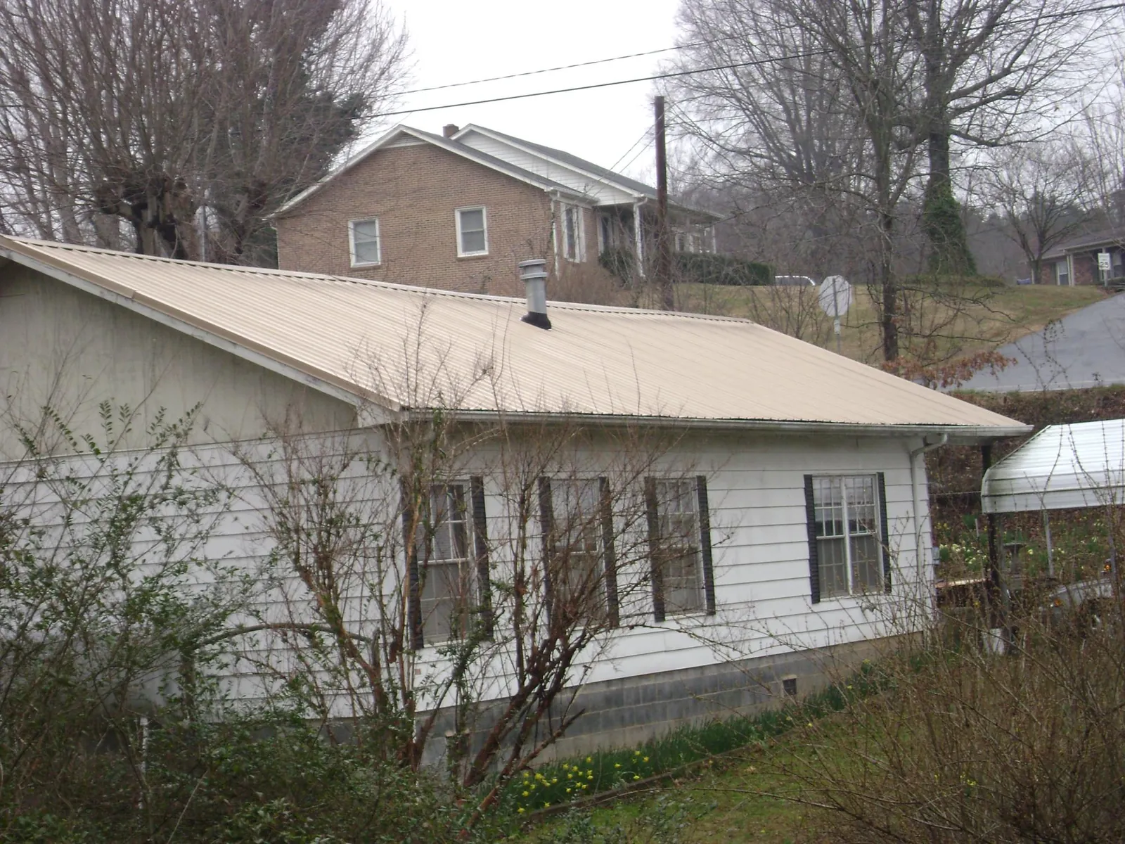 Tan metal roof on a white sided house set into a hillside — Commercial Roofing by Roofing Brothers in Victoria